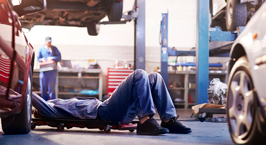 Mechanic under a car in an auto body shop