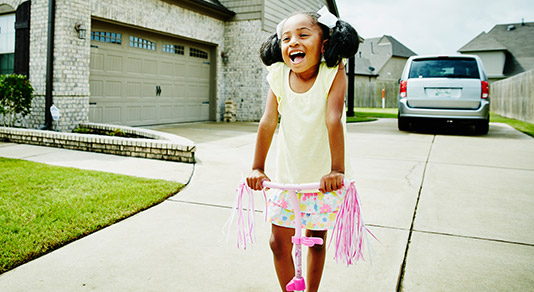 GIrl on bicycle in front of her home and car