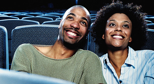 2 black couple watching a movie at a movie theatre