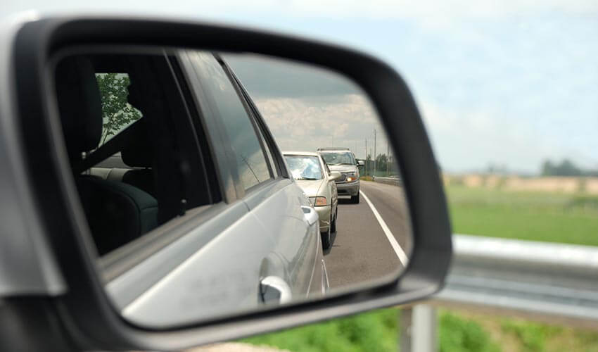 Reflection from car side view mirror showing two cars behind vehicle.