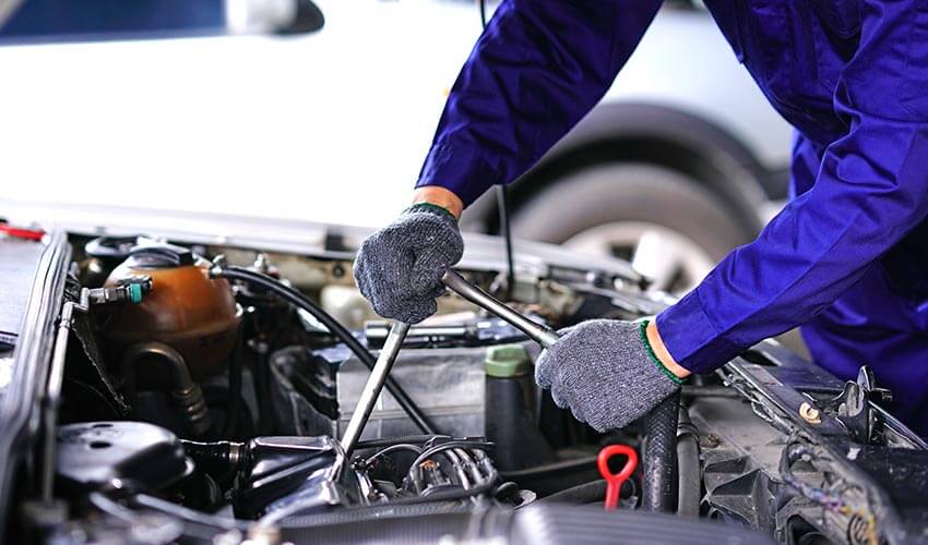 Mechanic fixing a car engine with a socket wrench.