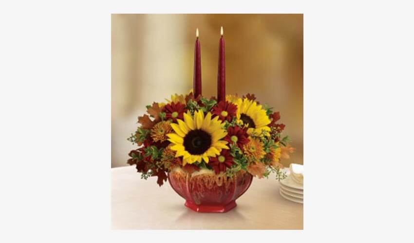 A bouquet of festive flowers in red and yellow with candles in the middle of the pot.