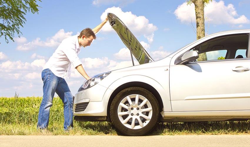 A man looking under hood of car in the summer.