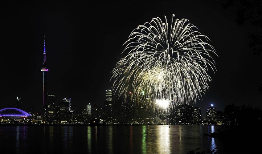 A spectacular display of fireworks over the Toronto Harbourfront, with the CN Tower, Rogers Centre and other buildings illuminating the skyline.