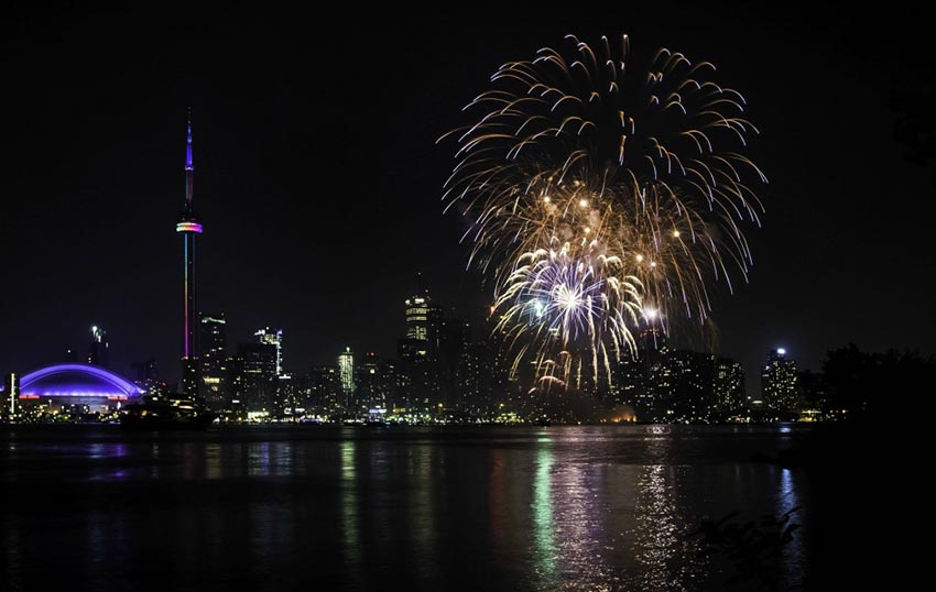 A spectacular display of fireworks over the Toronto Harbourfront, with the CN Tower, Rogers Centre and other buildings illuminating the skyline.