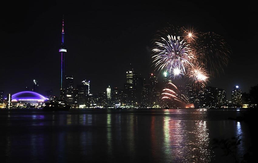 A spectacular display of fireworks over the Toronto Harbourfront, with the CN Tower, Rogers Centre and other buildings illuminating the skyline.