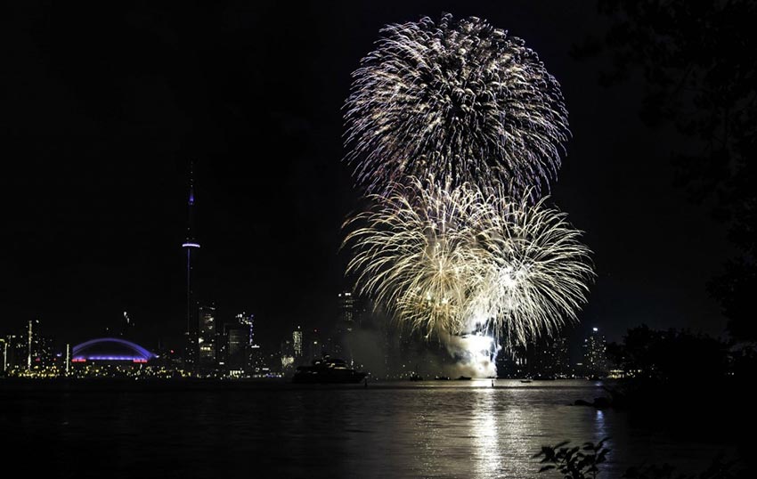 A spectacular display of fireworks over the Toronto Harbourfront, with the CN Tower, Rogers Centre and other buildings illuminating the skyline.