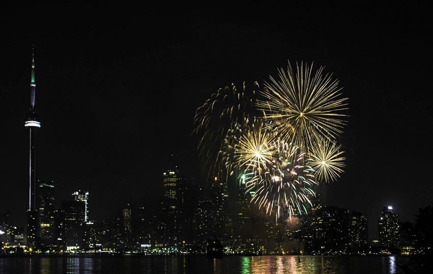 A spectacular display of fireworks over the Toronto Harbourfront, with the CN Tower, Rogers Centre and other buildings illuminating the skyline.