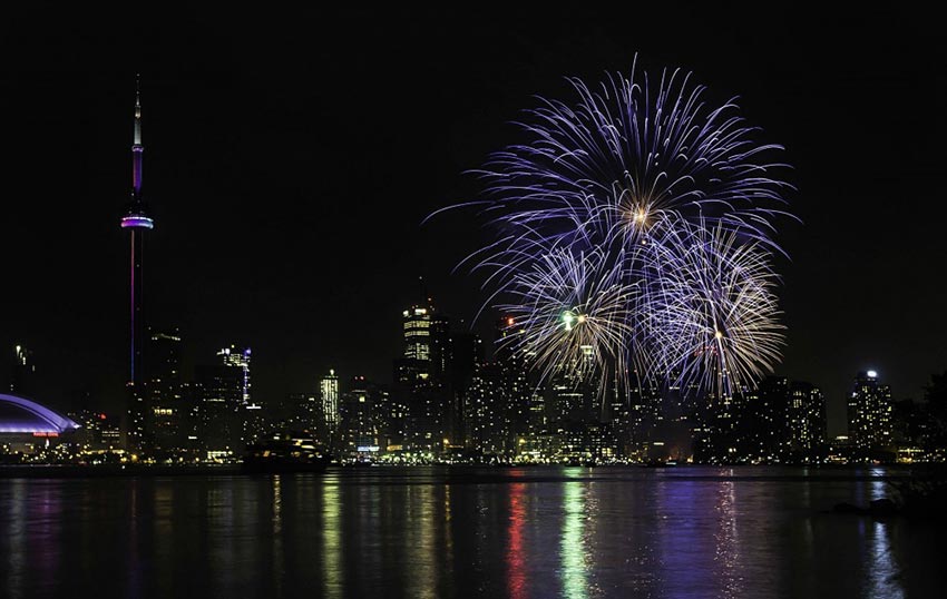 A spectacular display of fireworks over the Toronto Harbourfront, with the CN Tower, Rogers Centre and other buildings illuminating the skyline.