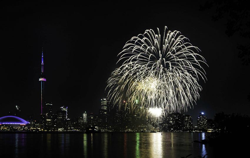 A spectacular display of fireworks over the Toronto Harbourfront, with the CN Tower, Rogers Centre and other buildings illuminating the skyline.