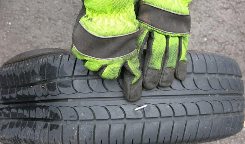 Hand pointing at an object embedded into tire, causing a flat.