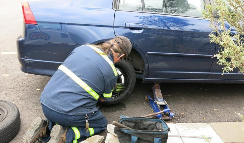 CAA tow truck driver putting on spare tire.