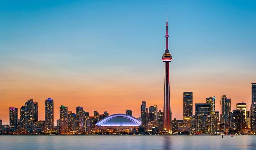 The CN Tower and the Rogers Centre in the Toronto Skyline among other buildings in the downtown core, with sun setting in the background.