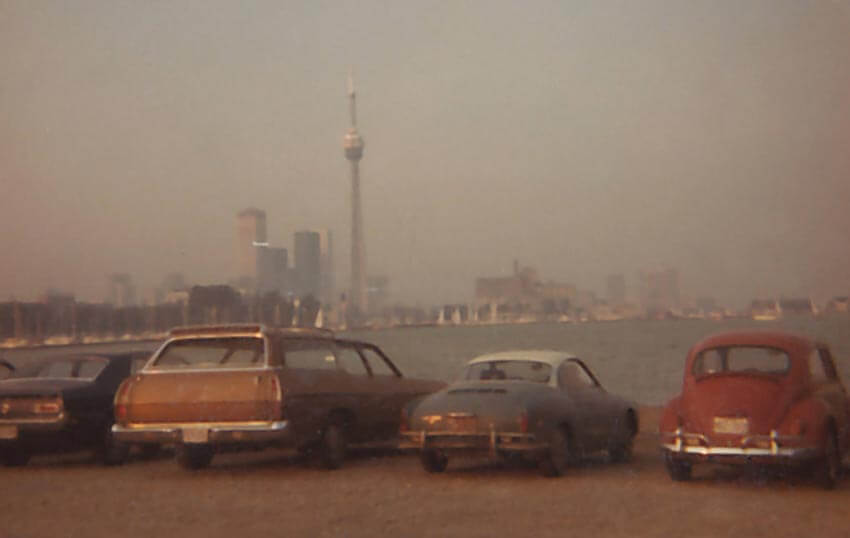 An old photograph of the CN Tower with old vintage cars parked in a row.