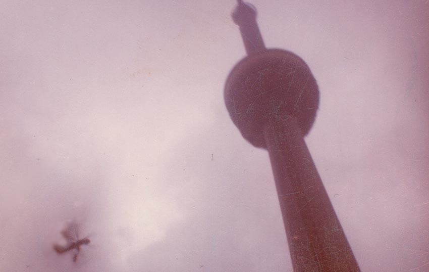 An old photograph of the CN Tower with a helicopter in the sky.
