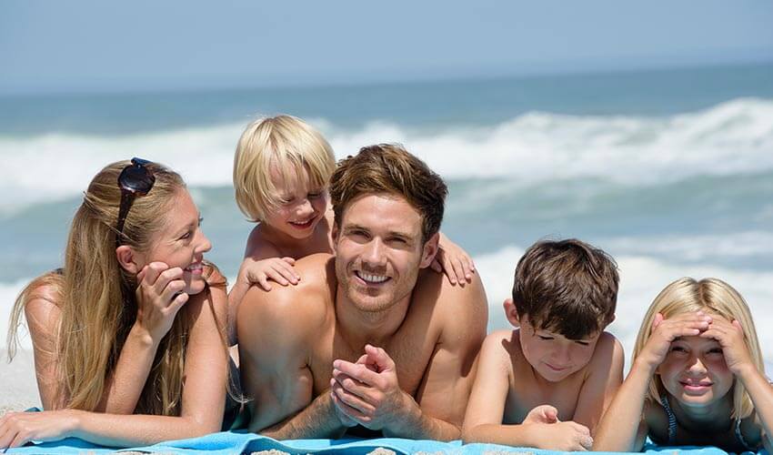 A family of five lying on the beach facing camera smiling.