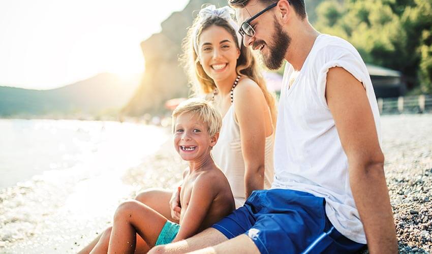A family of three sitting on the beach smiling.