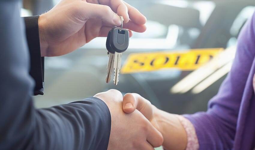 Close up of a car salesman holding car key with one hand and shaking the hand of a customer with another.