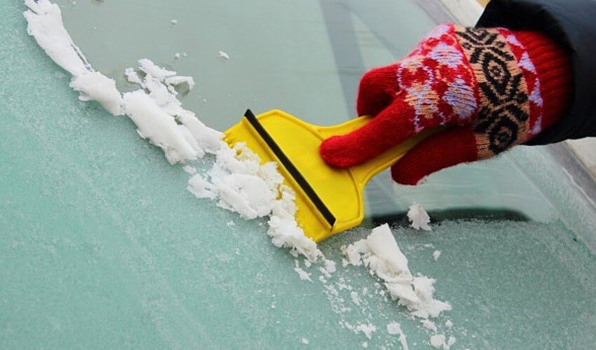 Close up of hand scraping ice from windshield.