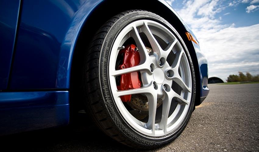 Low angle shot of front end of blue car, showing a close up of silver car rims