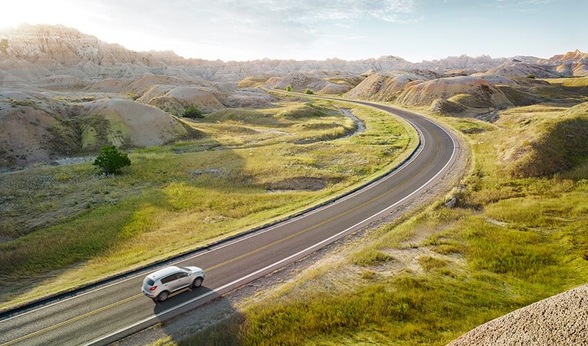 Aerial view of a SUV driving on a long winding road with hills in the background.