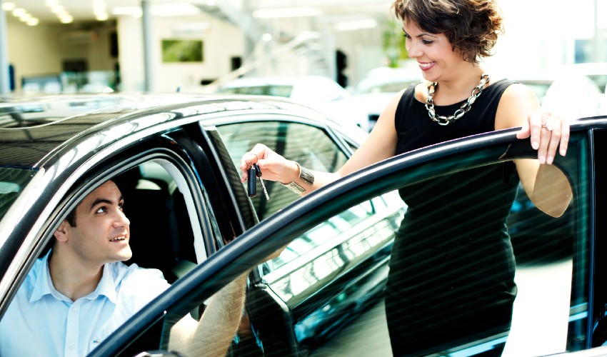 Sales woman handing over keys of new car to owner.