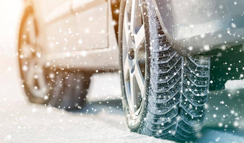 Close up of car with winter tires, snow in the background.