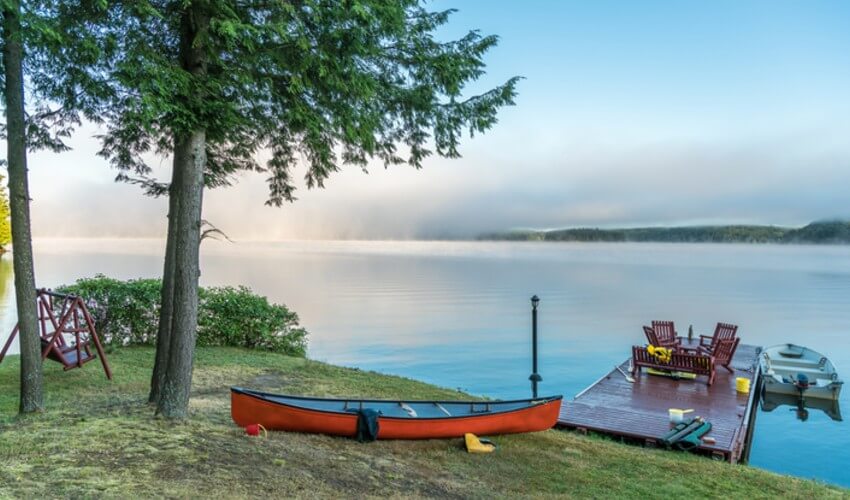A red canoe on the shoreline in front of a dock.
