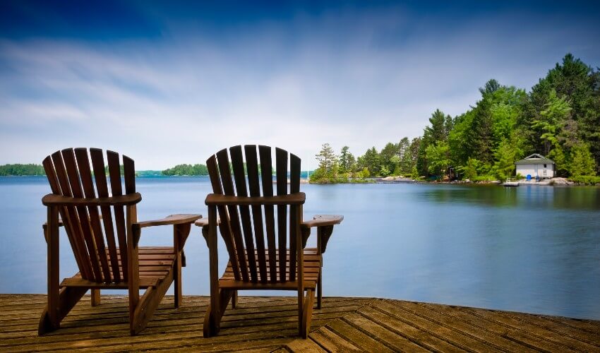 Two Muskoka chairs on a dock facing the water.