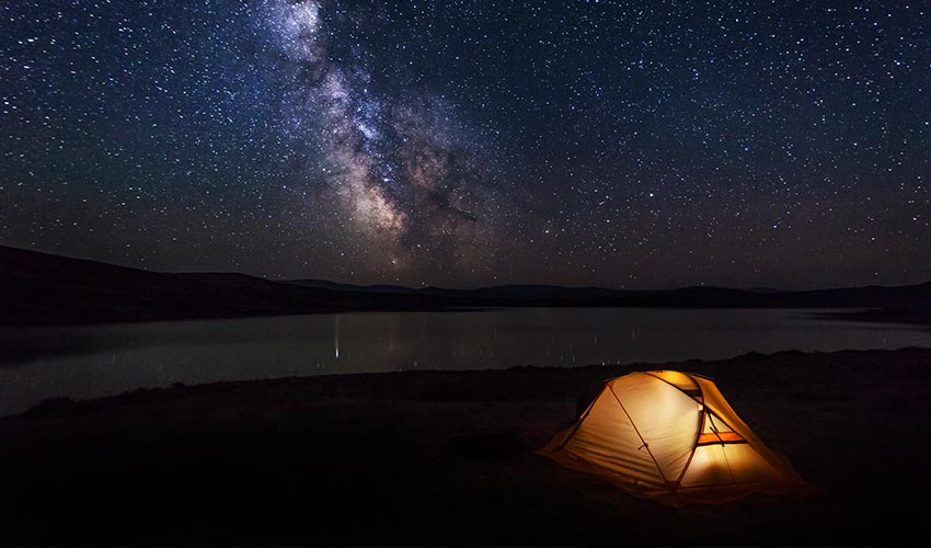 Star gazing in front of a lake with a tent set up.