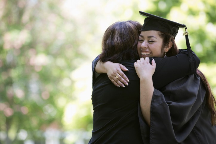 Hispanic mother hugging college graduate daughter