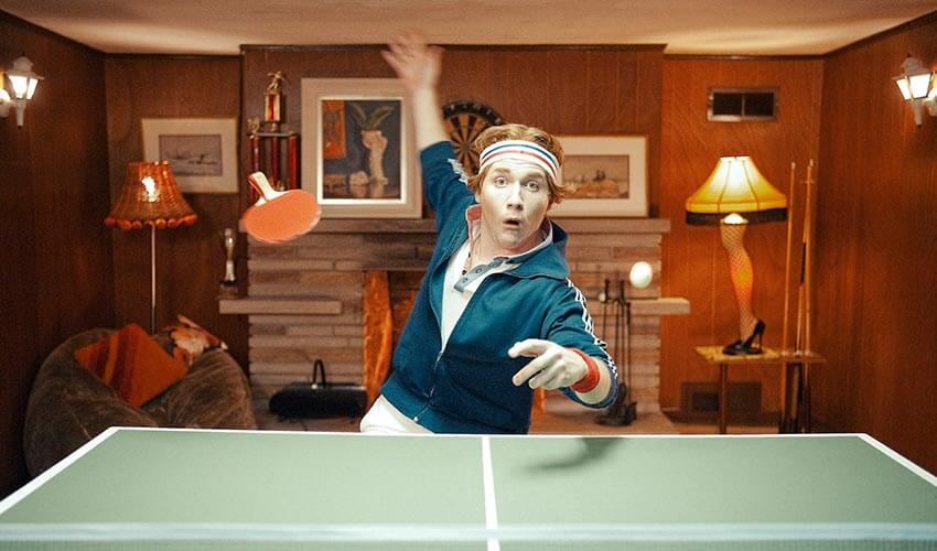 A man playing ping pong in a basement, dropping his racquet.