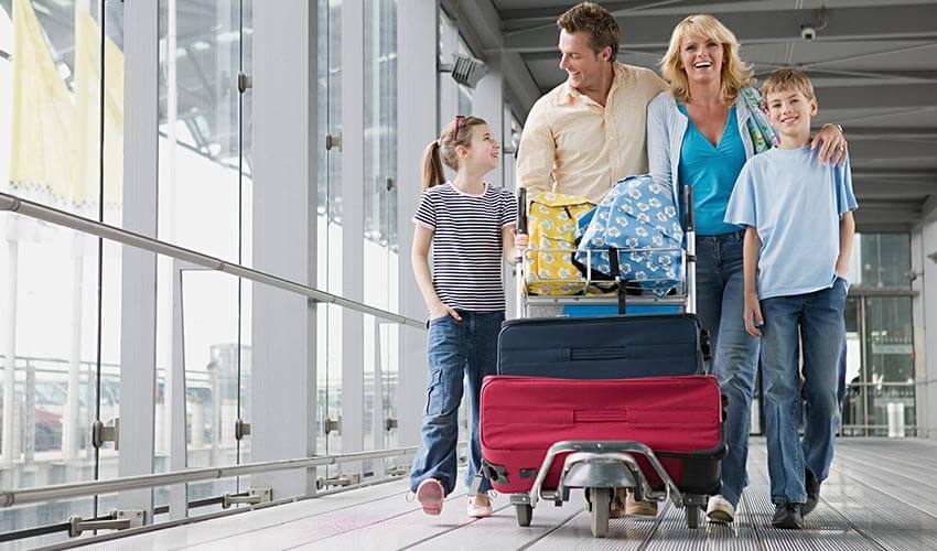 Family walking at an airport pushing a luggage cart.