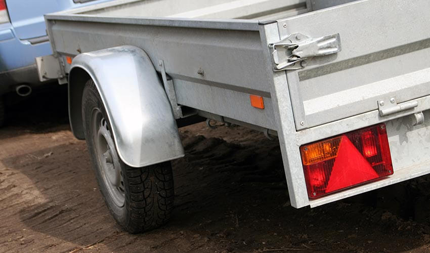Close up of a light blue car pulling a silver trailer.
