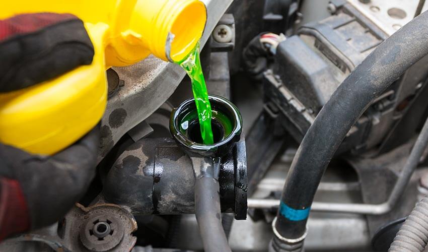 Close up of person pouring a green coloured coolant into coolant reservoir in car