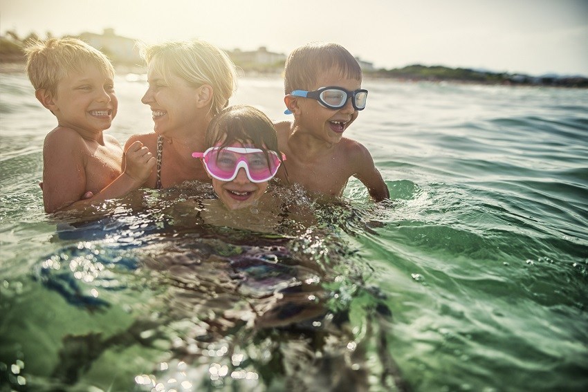 Mother with her three kids aged 7 and 10 are having fun splashing in sea waves. Family is having lovely tome todether. Candid smile and laughter. Sunny summer vacations day at sea.