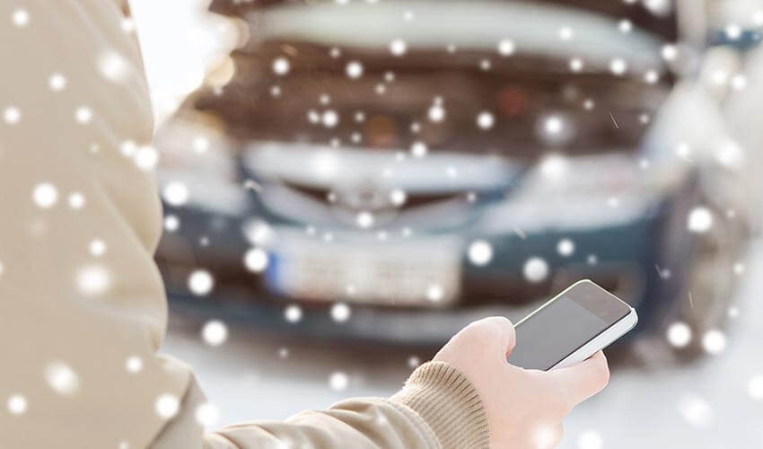 Stranded driver holding a phone with car in background during winter.