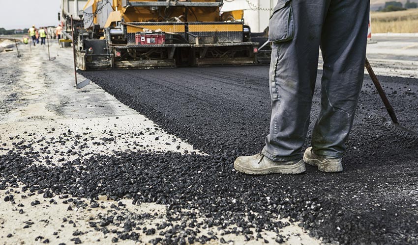 A construction worker laying asphalt on to a road.