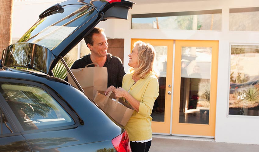 A Caucasian couple putting shopping bags into the trunk of a car.