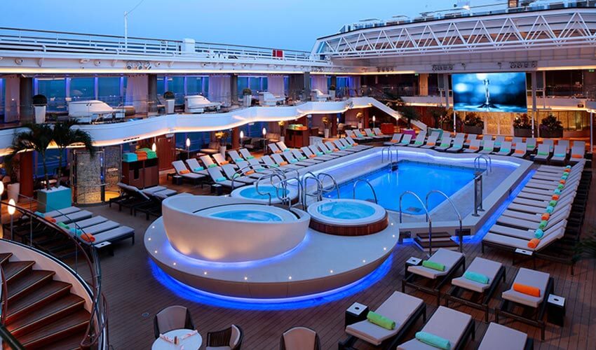 A pool on the cruise ship with lounge chairs, hot tubs, and large video screen.