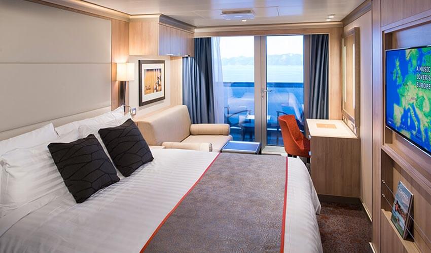 A suite on the cruise ship featuring a large bed, and balcony.