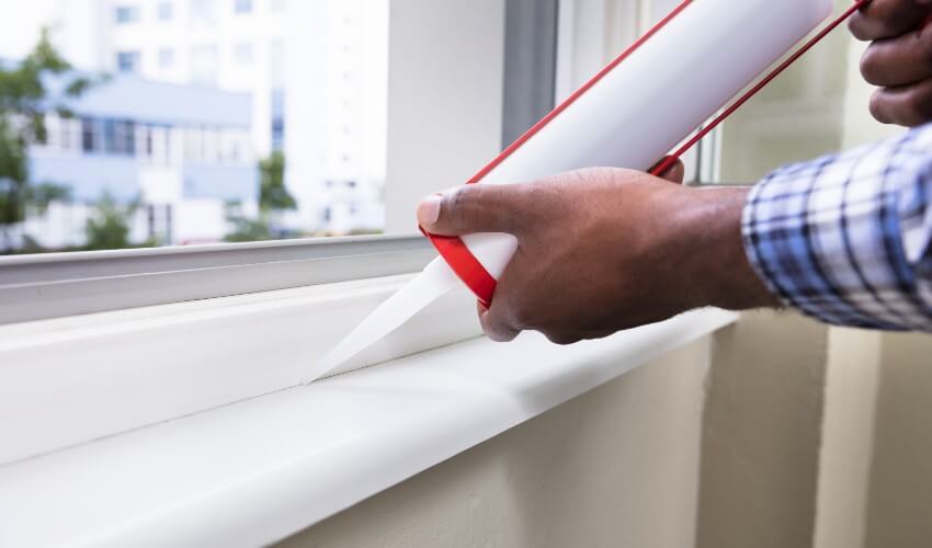 Close-up of hand applying silicone sealant on a window.