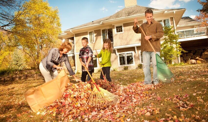 Two children helping family rake fall leaves in backyard.