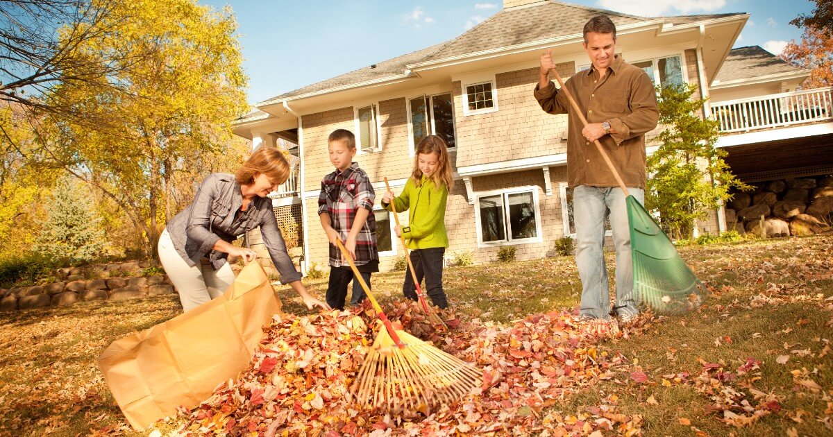 Two children helping family rake fall leaves in backyard.