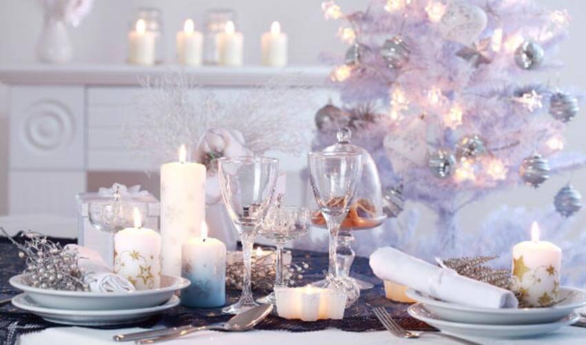 A modern floral arrangement on a dining table with table settings and white Christmas tree in background. 