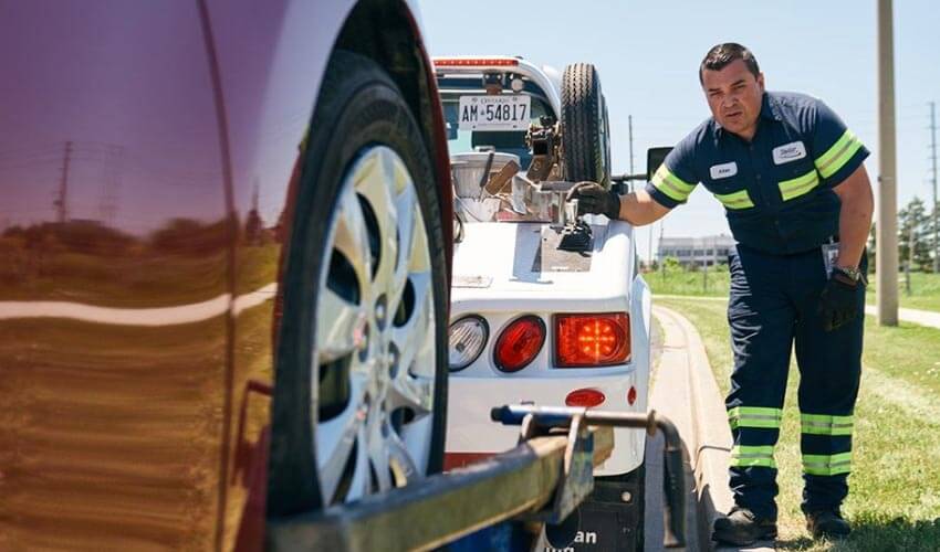 A CAA tow truck driver putting a stalled vehicle on to a flat bed tow truck
