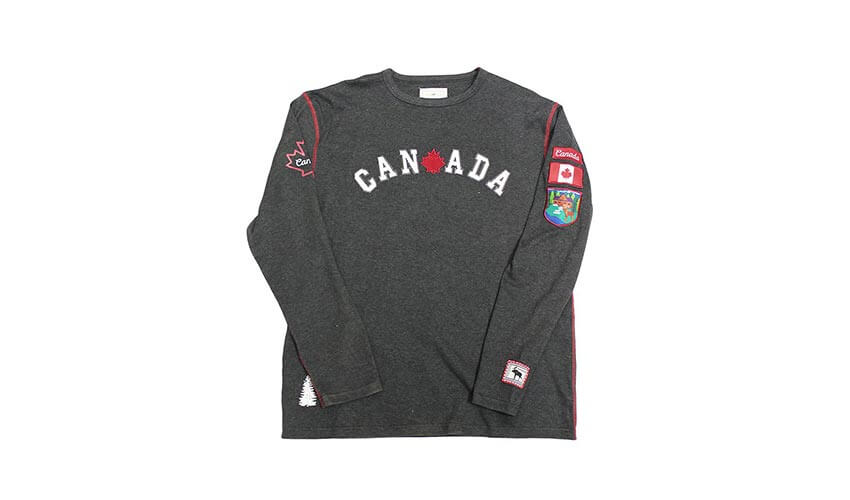 A men's grey long-sleeve shirt with the word "Canada" in the front and patches on the upper sleeve.