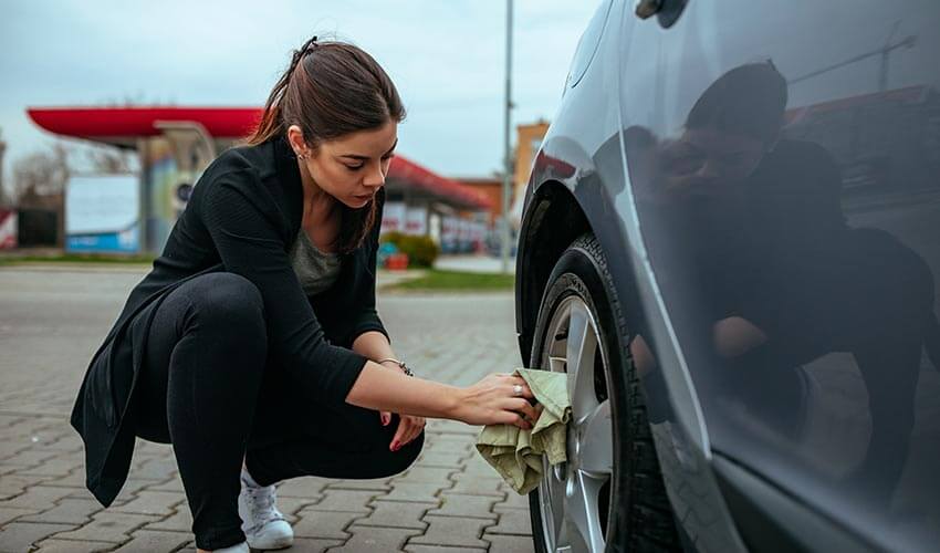 Woman cleaning wheels of car near gas station.