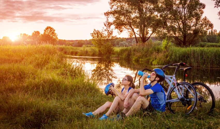 Two cyclists resting by their bikes having a water break under a beautiful sunset.