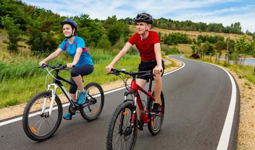 Two cyclists riding on a roadway on a beautiful day.